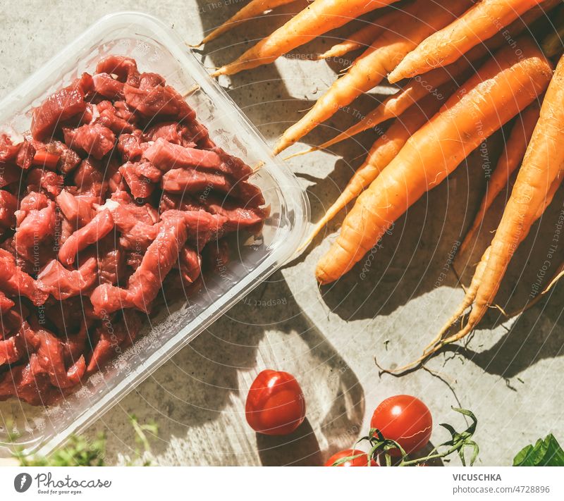 Nahaufnahme von rohem geschnittenem Fleisch in einem Plastikbehälter, Karotten und Tomaten abschließen geschnittenes Fleisch Kunststoff Container Beton Küche