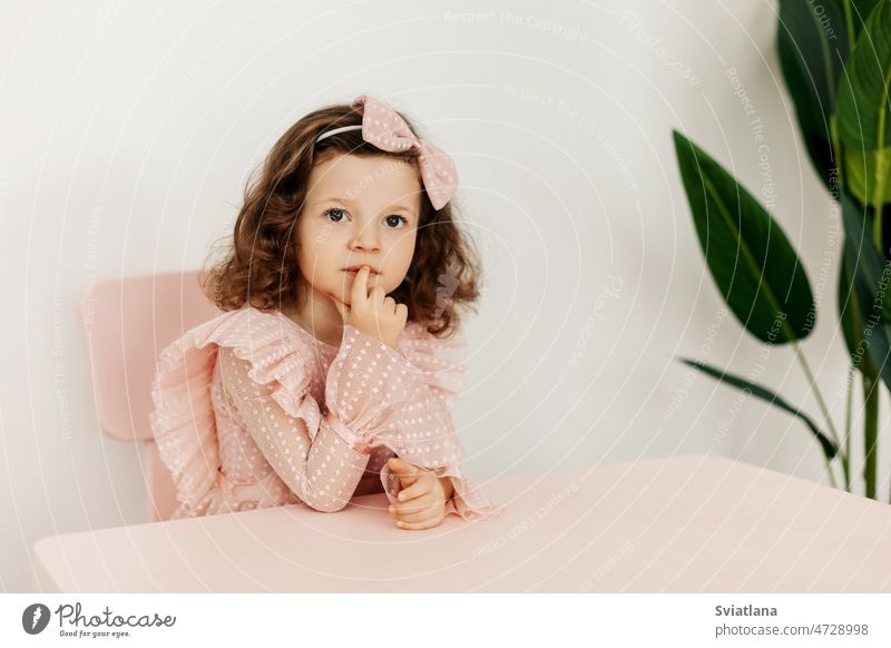 Porträt eines kleinen Mädchens in festlicher Kleidung, das nachdenklich an einem Tisch sitzt wenig Sitzen Blick Denken Kind Schreibtisch neugierig jung Frau
