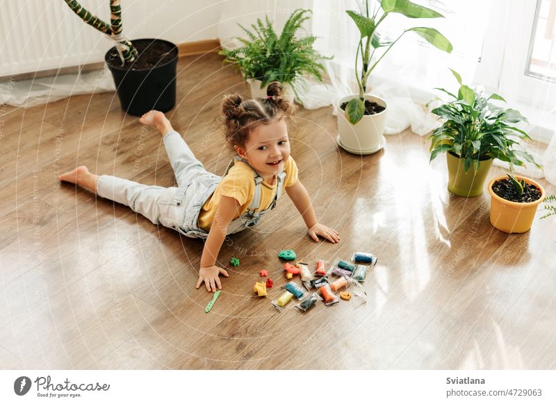 Ein reizendes kleines Mädchen modelliert aus farbiger Knete auf dem Boden. Hausunterricht, kreative Freizeitgestaltung mit Kindern Baby spielen heimwärts