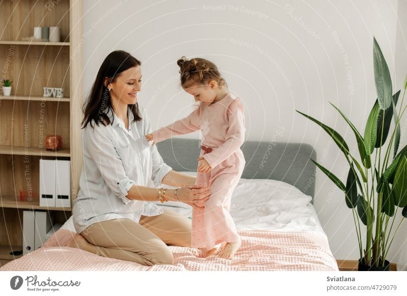 Eine junge Mutter spielt mit ihrem Baby im Schlafzimmer. Glückliche, liebevolle Familie. Mama Bett Spielen Spaß Mädchen Kind Porträt lustig Fröhlichkeit