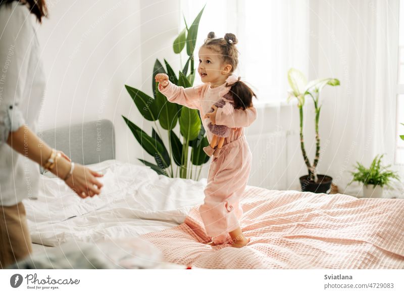 Ein reizendes kleines Mädchen spielt tagsüber mit ihrer Mutter auf dem Bett mit Puppen. Mutterschaft, Fürsorge, gemeinsame Zeit Tochter Mama spielen Tag hübsch