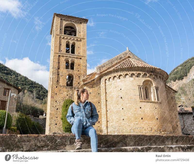 Schöne junge Frau, die in einem schönen mittelalterlichen Dorf sitzt und entspannt Beget besucht, mit der romanischen Kirche von Saint Christopher im Hintergrund