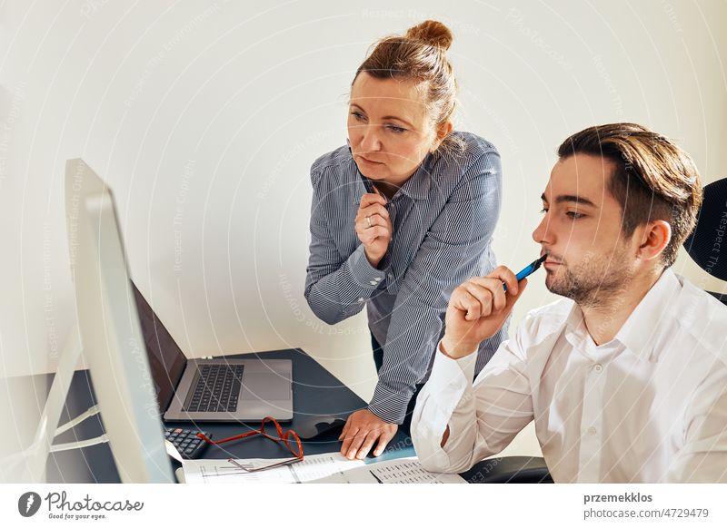 Zwei Geschäftsleute diskutieren über Finanzdaten und schauen auf den Computerbildschirm. Geschäftsfrau im Gespräch mit jungen männlichen Mitarbeiter im Büro. Menschen Unternehmer im Gespräch arbeiten zusammen