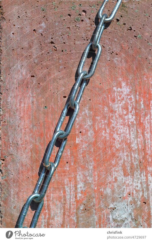 Kette aus Metallgliedern vor rotem Hintergrund Glied Kettenglied MAuer Beton Wand Halt Festigkeit Stabilität Rost Zusammenhalt Eisen Stahl Verbundenheit