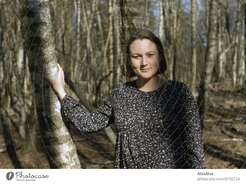 Analoges Portrait einer jungen, schwangeren Frau, die in einem Laubwald steht und sich an einem Baum abstützt Lächeln kraftvoll Gras Waldboden Bäume Model