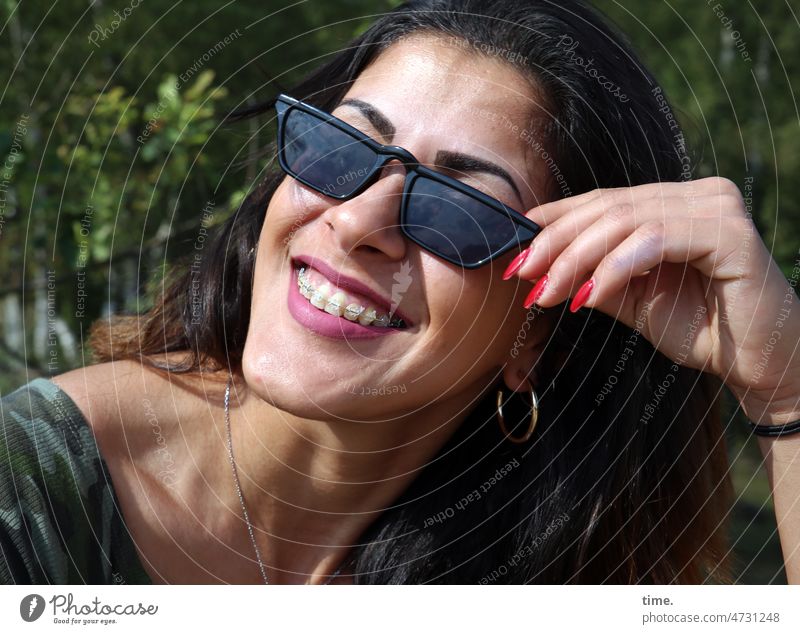 Frau mit Sonnenbrille frau feminin lächeln lachen schmuck zahnspange dunkelhaarig langhaarig draußen sonnig