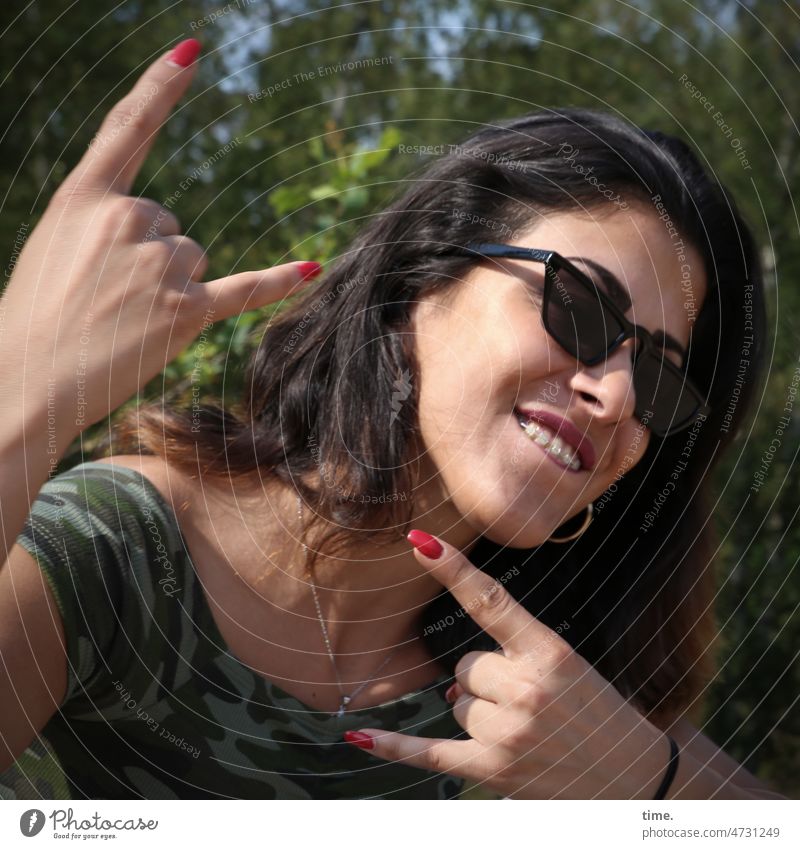 Frau mit Pommesgabel (Wacken Style) frau Sonnenbrille handzeichen t-shirt langhaarig feminin dunkelhaarig natur sonnig bäume zahnspange halskette
