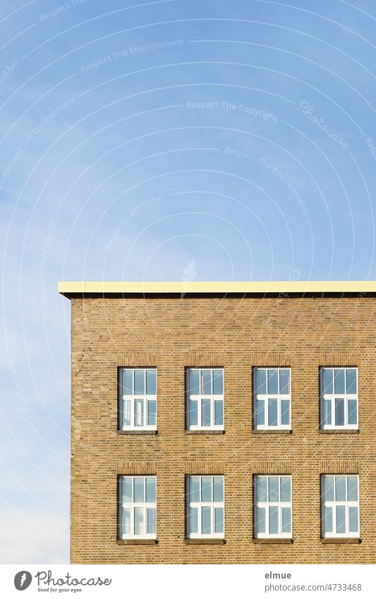 Teilansicht eines Industriegebäudes mit Fenstern, Klinkerfassade und Flachdach vor blauem Himmel / arbeiten Werksgebäude Ziegelsteine Geometrie himmelblau