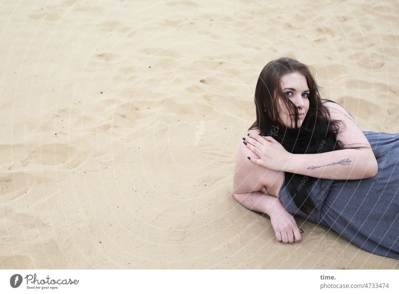 liegende Frau im Sand schauen frau kleid feminin langhaarig dunkelhaarig tattoo sand aufstützen abstützen skeptisch