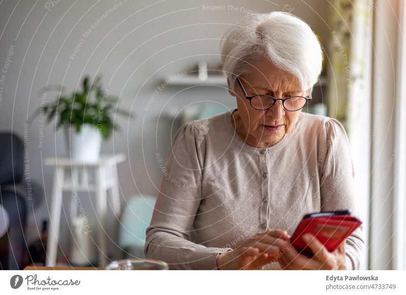 Ältere Frau benutzt Mobiltelefon zu Hause Brille allein häusliches Leben älter Oma Großmutter graue Haare heimwärts im Innenbereich Lifestyle reif alt