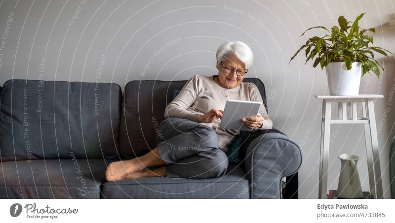 Ältere Frau benutzt ein digitales Tablet zu Hause Tablette digitales Tablett online Internet modern Technik & Technologie Mitteilung Anschluss Wohnzimmer Brille