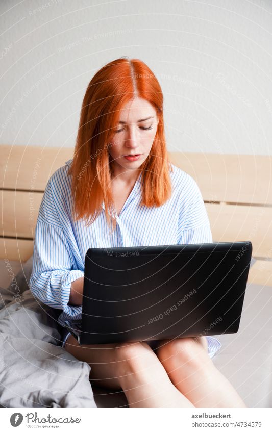 Junge Frau, die von zu Hause aus arbeitet, sitzt auf einem Bett mit einem Laptop-Computer Sitzen Schlafzimmer Arbeit von zu Hause aus benutzend Tippen heimwärts