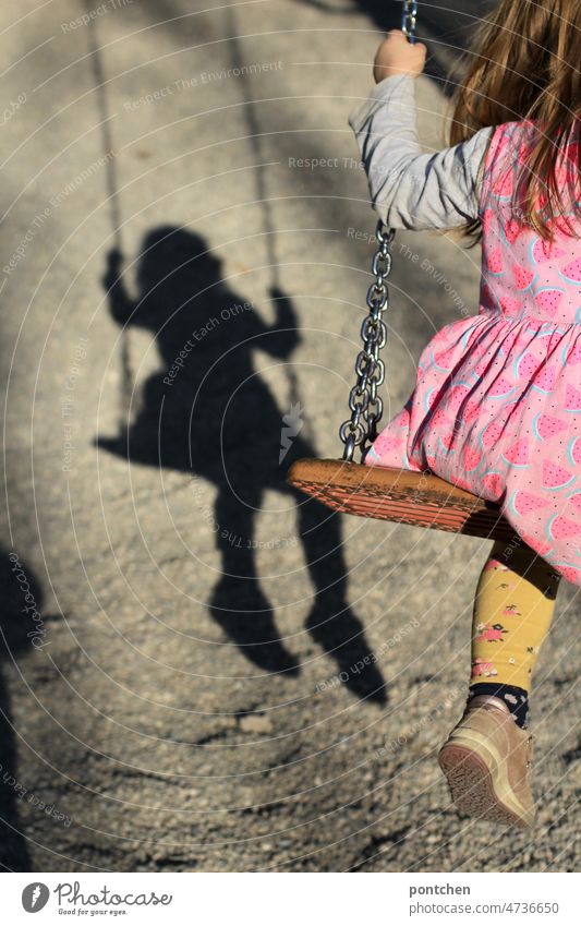 Kindheit in Schatten. Ein Kind auf einer Schaukel wirft einen Schatten. Belastete Kindheit. symbolbild. Corona, Pandemie kind schaukeln schatten belastung