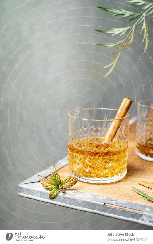 Glas Whiskey mit Zimtstange unter Pflanzenzweig kleben Würzig starker Alkohol Schnaps Kristalle dienen Glaswaren Gewürz Weinbrand Eckstoß Geschmack Bourbon