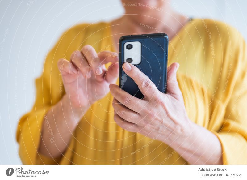 Crop erwachsene Frau mit Smartphone gegen weiße Wand benutzend Talkrunde Internet Browsen online Anschluss soziale Netzwerke Nachricht Mobile Telefon Gerät reif