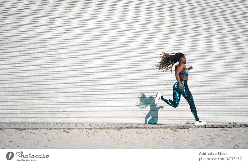 Aktive schwarze Frau, die während des Trainings auf der Strandpromenade läuft laufen Herz physisch passen Bewegung Fitness aktiv Rastalocken Laufsteg