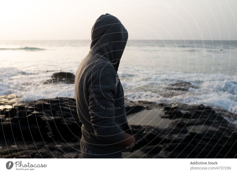 Anonymer Mann mit Kapuze steht am Strand bewundern Meer Urlaub nachdenken Harmonie Freiheit Gelassenheit Ausflug männlich Sand Insel Ufer Küste Meeresufer