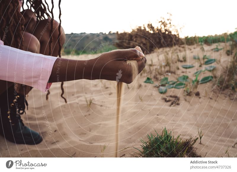 Crop schwarze Frau mit einer Handvoll Sand am Meer verschütten Strand Meeresufer Sommer Sonnenuntergang Abend eingießen ethnisch Afroamerikaner Natur Küste