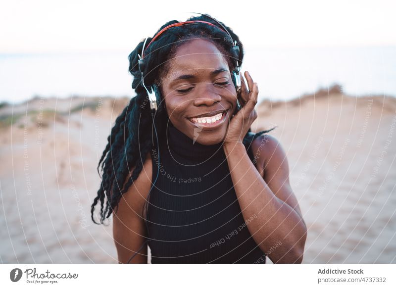 Unbekümmerte schwarze Frau hört am Strand Musik zuhören Tanzen Gesang Kopfhörer Sommer Meeresufer Spaß haben ethnisch Afroamerikaner sorgenfrei Freiheit