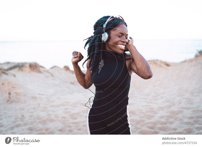 Unbekümmerte schwarze Frau hört am Strand Musik zuhören Tanzen Gesang Kopfhörer Sommer Meeresufer Spaß haben ethnisch Afroamerikaner sorgenfrei Freiheit