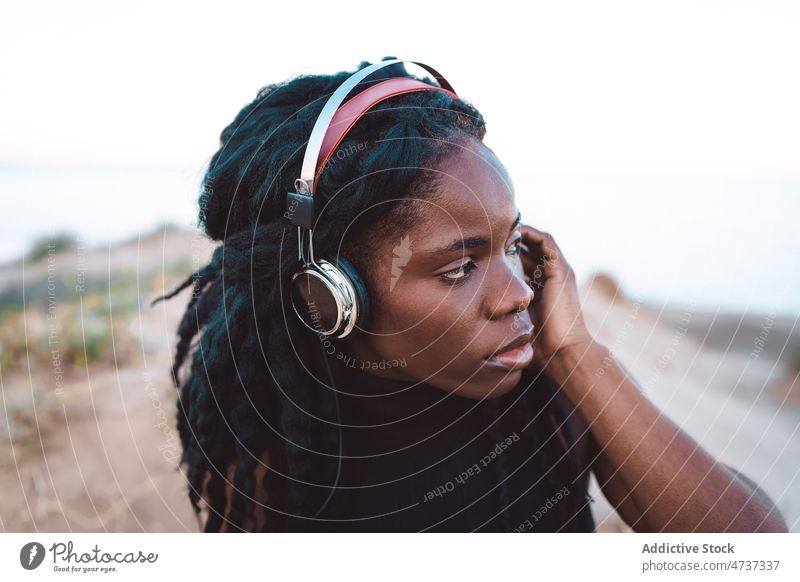 Unbekümmerte schwarze Frau hört am Strand Musik zuhören Gesang Kopfhörer Sommer ernst Meeresufer konzentriert ethnisch Afroamerikaner sorgenfrei Freiheit