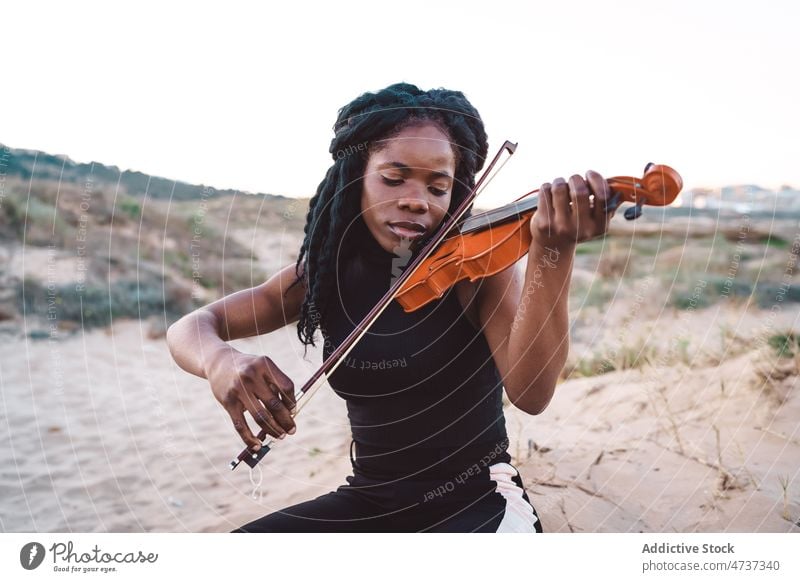Verträumte schwarze Frau spielt Geige am Meer spielen verträumt Musik Strand Musiker Melodie Instrument Augen geschlossen ethnisch Afroamerikaner genießen