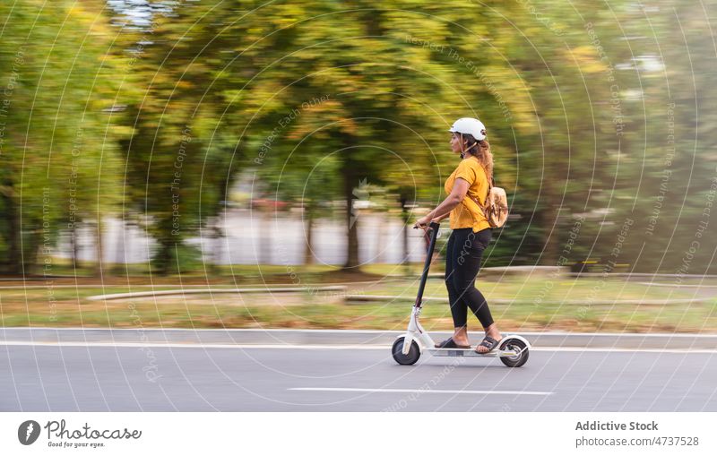 Lächelnde schwarze Frau fährt Roller in einer Gasse Tretroller Mitfahrgelegenheit Schutzhelm Park behüten umweltfreundlich Aktivität elektrisch Weg Laufsteg