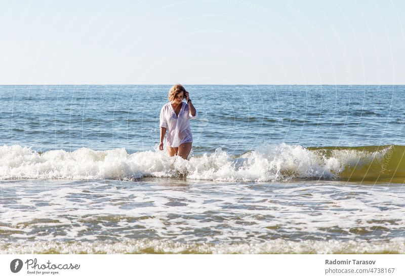 Junge blonde Frau in einem nassen weißen Hemd kommt in der Nähe des Meeresufers aus dem Wasser im Freien Wellen Person jung Sommer MEER Behaarung Natur Glück