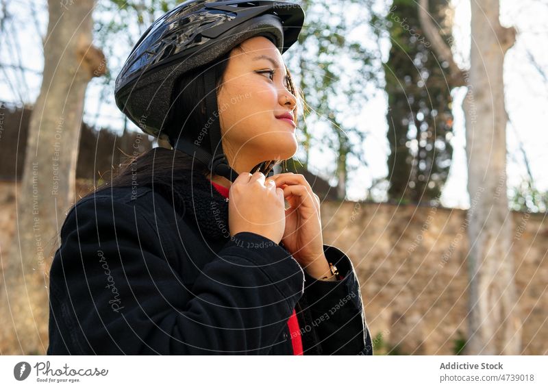 Stilvolle ethnische Frau, die einen Helm zum Fahrradfahren aufsetzt befestigen Schutzhelm angezogen Aktivität Hobby Park üben vorbereiten aktiv lässig jung