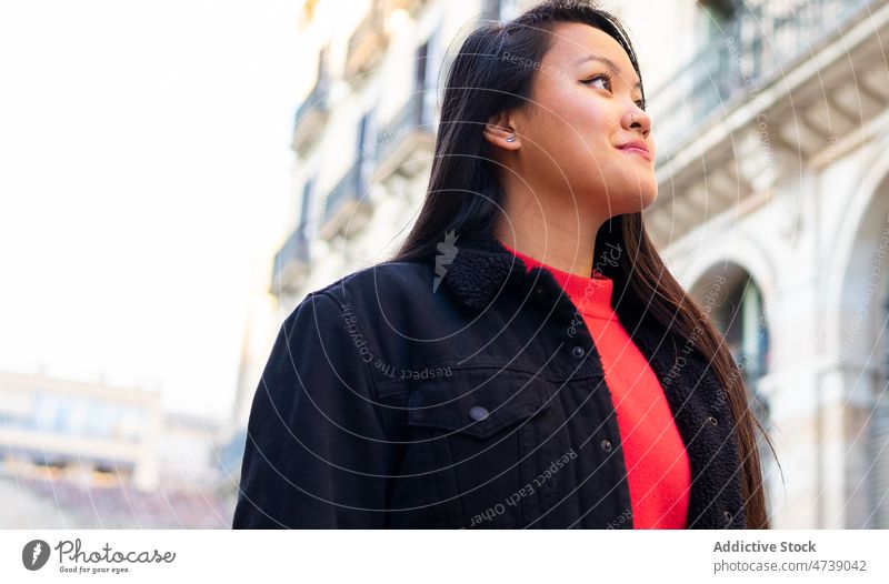 Lächelnde asiatische Frau auf der Straße stehend während alter Gebäude bewundern sorgenfrei beobachten Vorschein positiv Großstadt erkunden Persönlichkeit