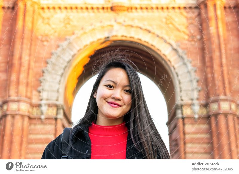 Lächelnde asiatische Frau auf der Straße stehend während alter Gebäude bewundern sorgenfrei beobachten Vorschein positiv Großstadt erkunden Persönlichkeit