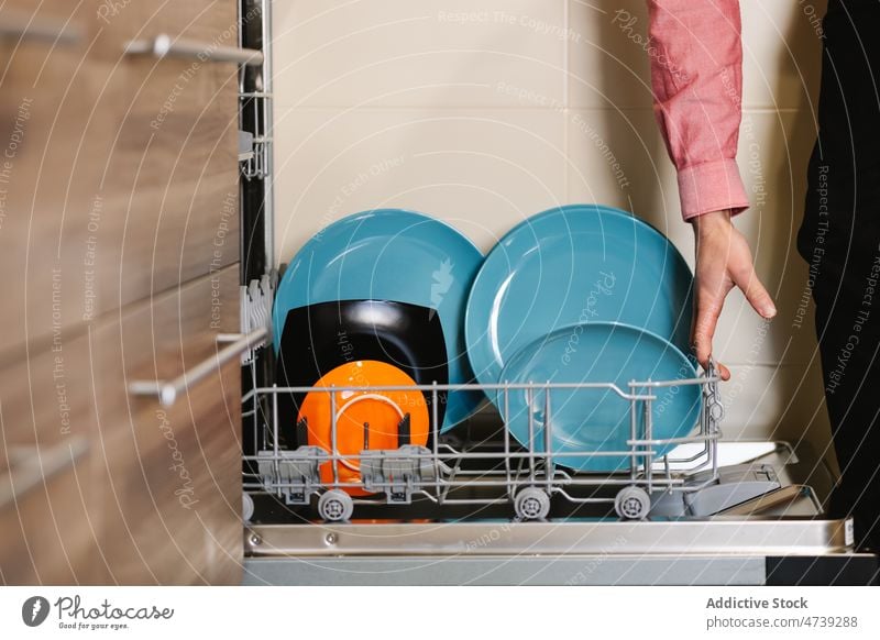 Crop-Mann räumt in der Küche Keramikteller in die Spülmaschine laden Geschirrspüler Teller Waschen Gerät Haushalt Hausarbeit Hygiene Küchengeräte modern