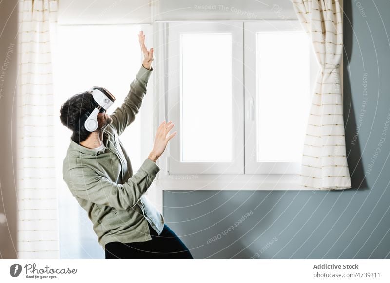 Junger Mann erkundet den Cyberspace mit einer VR-Brille zu Hause Virtuelle Realität Lächeln Erfahrung Innovation gestikulieren simulieren unterhalten digital