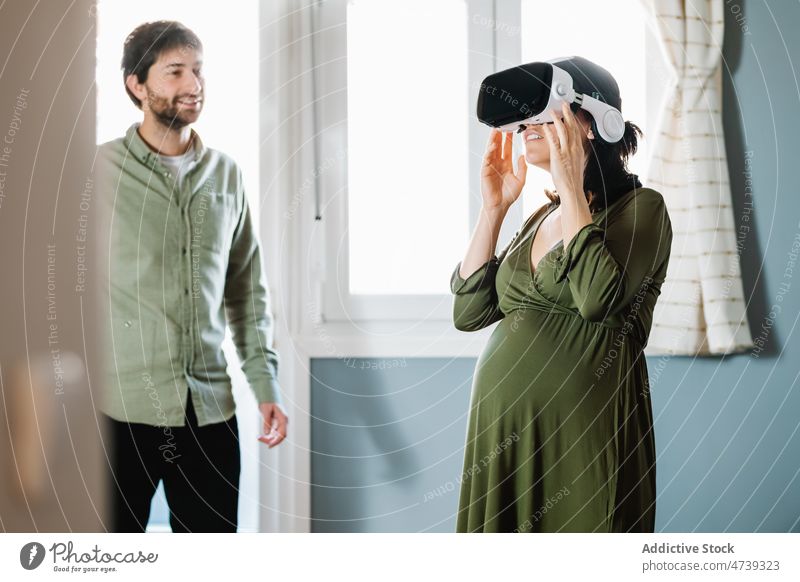 Glückliches schwangeres Paar mit VR-Brille, das in der Nähe des glücklichen Ehemanns steht Virtuelle Realität Partnerschaft erstaunt erkunden Lächeln