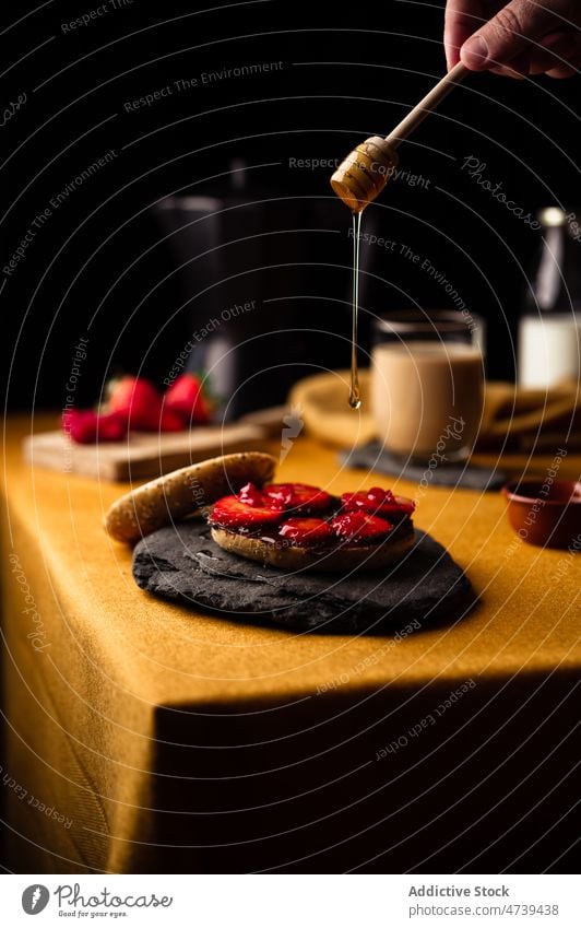 Person gibt Honig vom Holzlöffel auf den Bagel Liebling Erdbeeren Frühstück süß frisch lecker Schokolade dienen Löffel Schliere Kaffee Moka-Topf Dessert