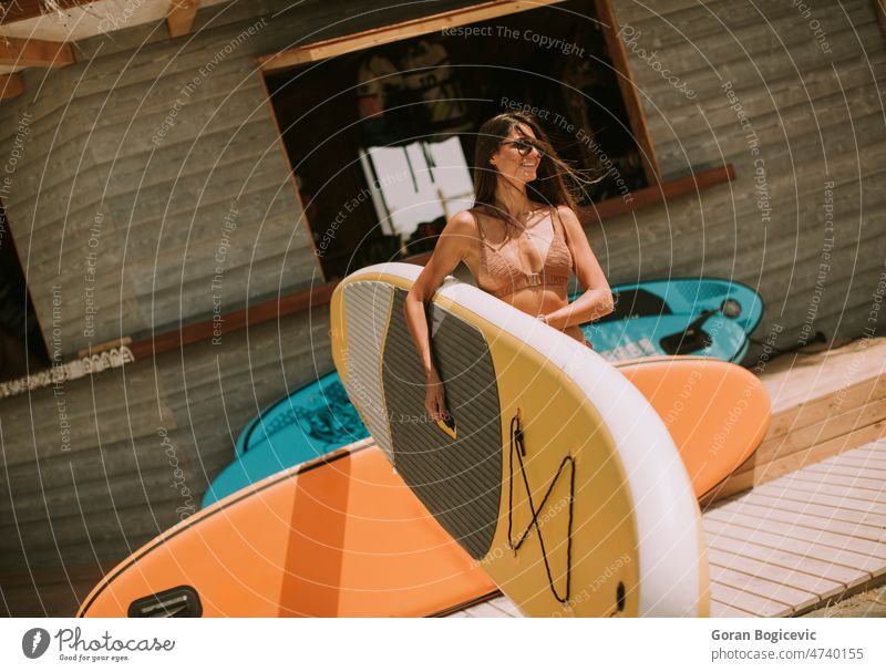 Junge Frau mit Paddelbrett am Strand an einem Sommertag attraktiv schön Bikini Holzplatte Küste Tag passen Freunde Freundschaft Spaß Glück Lifestyle Meer