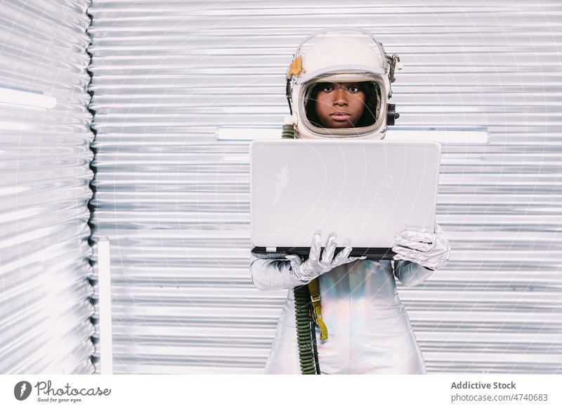 Schwarzer Astronaut surft auf Laptop im Raumschiff Frau Raumanzug Schutzhelm Kosmonaut Browsen online Internet Surfen Missionsstation Uniform modern Sicherheit