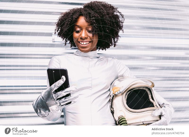Glücklicher schwarzer Astronaut, der im Raumschiff auf seinem Smartphone surft Frau Raumanzug Schutzhelm Kosmonaut froh Browsen online Internet Surfen Lächeln