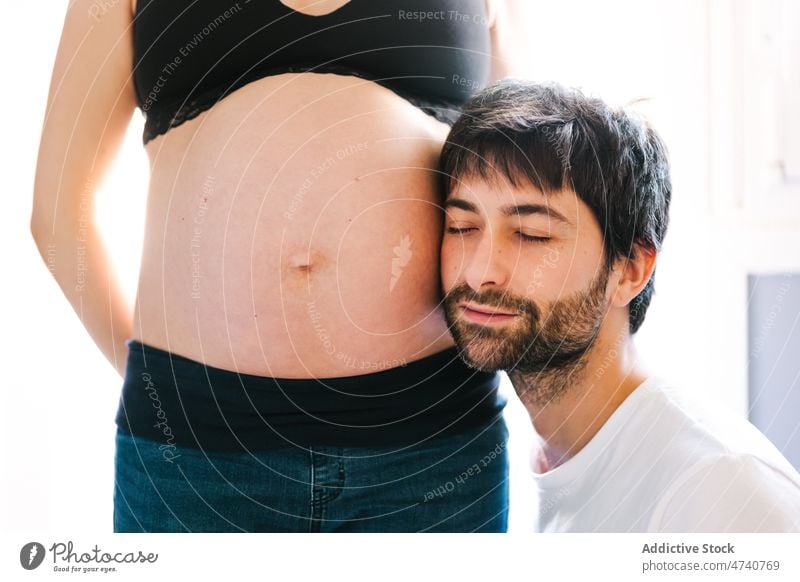 Sanftmütiger Mann hört dem Bauch einer schwangeren Frau zu Paar zuhören Ehemann Schwangerschaft vorwegnehmen verträumt berühren Mutter Vater Ehefrau