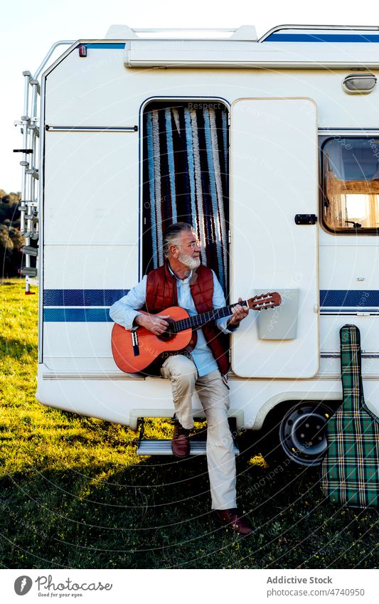 Älterer Mann spielt Gitarre in der Tür eines Wohnmobils rv sitzen Türöffnung Natur Autoreise Senior Instrument Hobby spielen Gesang Melodie Fähigkeit Talent