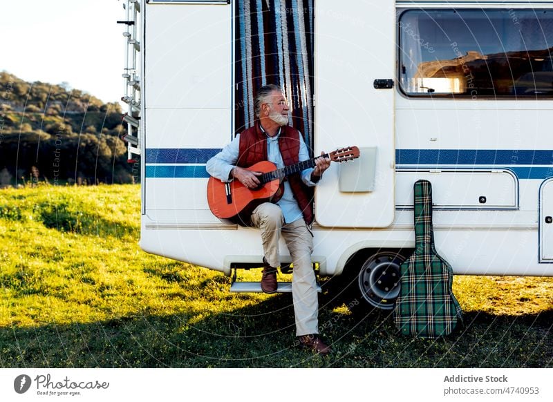 Älterer Mann spielt Gitarre in der Tür eines Wohnmobils rv sitzen Türöffnung Natur Autoreise Senior Instrument Hobby spielen Gesang Melodie Fähigkeit Talent