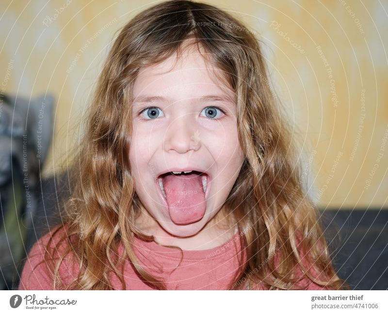 Mädchen mit rausgestreckter Zunge Kind Kindheit Blick in die Kamera lockiges haar Locken Schulkind böse Mimik Gesicht Kindergesicht Blick nach vorn Augenfarbe