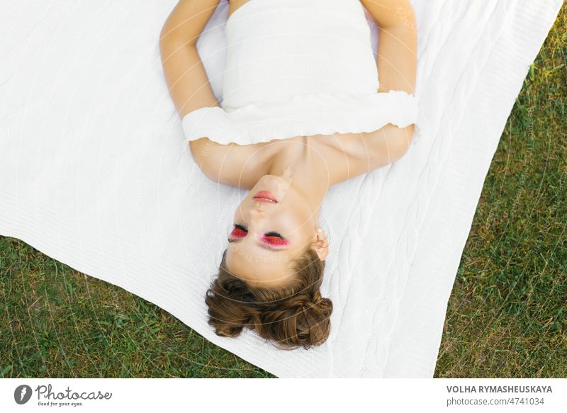 Eine schöne junge Frau mit hellen Make-up im Stil der "Wassermelone" liegt mit geschlossenen Augen auf einer Decke im Freien im Sommer Person hübsch Gesicht