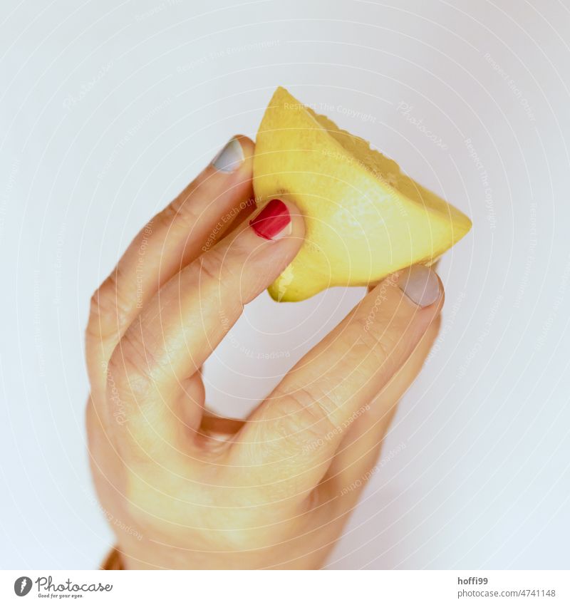 eine halbe Zitrone in einer Hand mit verschiedenfarbig  lackierten Fingernägeln Zitrusfrüchte frisch gelb Frucht sauer Vitamin C zitronengelb