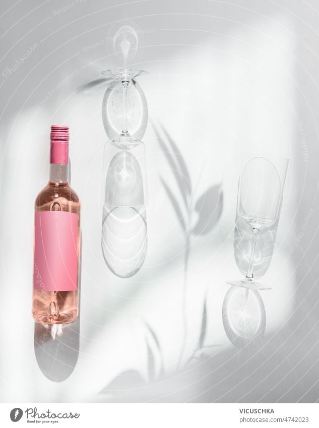 Rose Weinflasche und zwei Weingläser auf weißem Hintergrund mit Sonnenlicht Rosenwein weißer Hintergrund leer rosa Musteretikett Schatten modern Weinkonzept