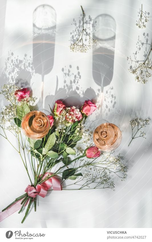 Champagnergläser mit Rosenwein und schönem Blumenstrauß mit Rosen zwei weißer Hintergrund Sonnenlicht Schatten Feier Getränke Draufsicht Blütezeit Textfreiraum