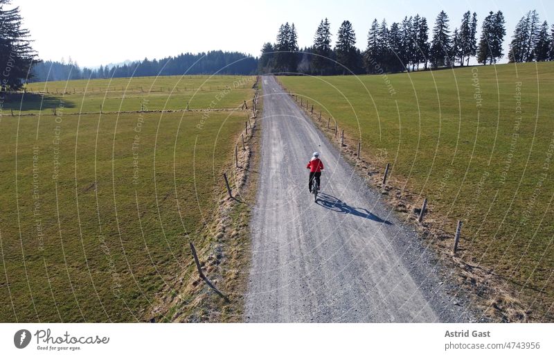 Luftaufnahme mit einer Drohne von einer Fahrradfahrerin auf einer einsamen Straße mit Schatten luftaufnahme drohnenfoto frühling sport radfahren fahrrad frau