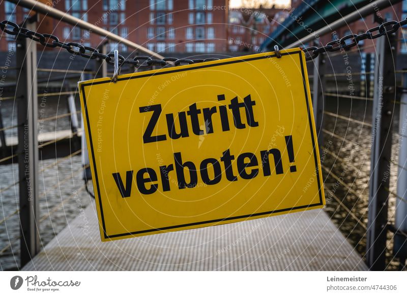 Zutritt Verboten Schild mit schwarzer Schrift und gelben Hintergrund an einer Kette hängend vor einem anleger an einem Gewässer Warnung halt Stopp Sperre