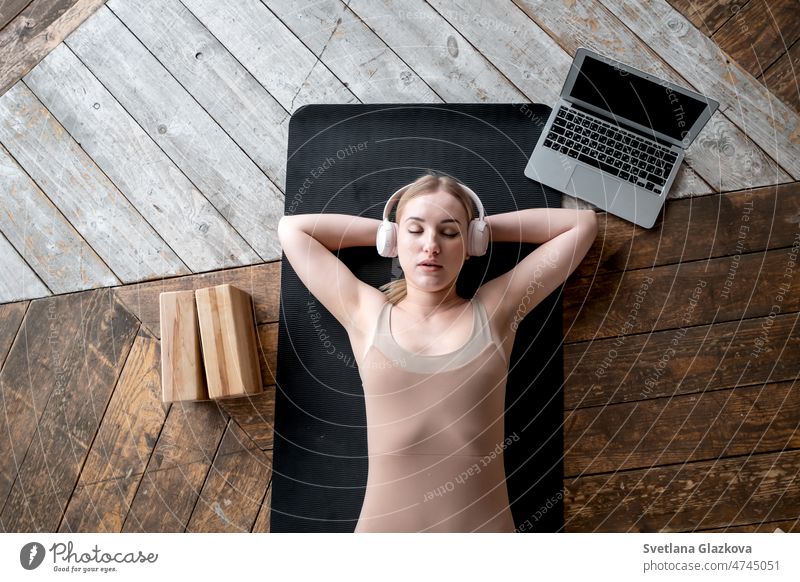 Frau geschlossen Augen liegt auf Sportmatte auf dem Boden. Tragen Sie Kopfhörer hören Musik Meditation Mental Health Pflege Wellness Yoga Myofasziale Entspannung