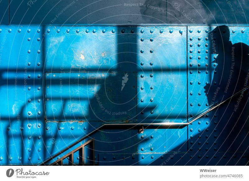 Der Schatten eines Mannes an einer sehr blauen Wand aus Metall, offenbar an einer Treppe Nieten Blech Stahl Eisen Farbe Geländer Muster Passant Unbekannter